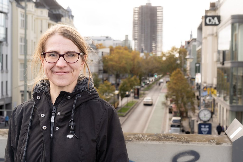 Franziska Brychy ist frontal von der Hüfte aufwärts zu sehen, im Hintergrund die Schloßstraße in Steglitz-Zehlendorf mit dem Steglitzer Kreisel.